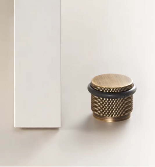 Angle view of knurled brass door stopper showing precision-machined knurled barrel and sturdy floor mounting base